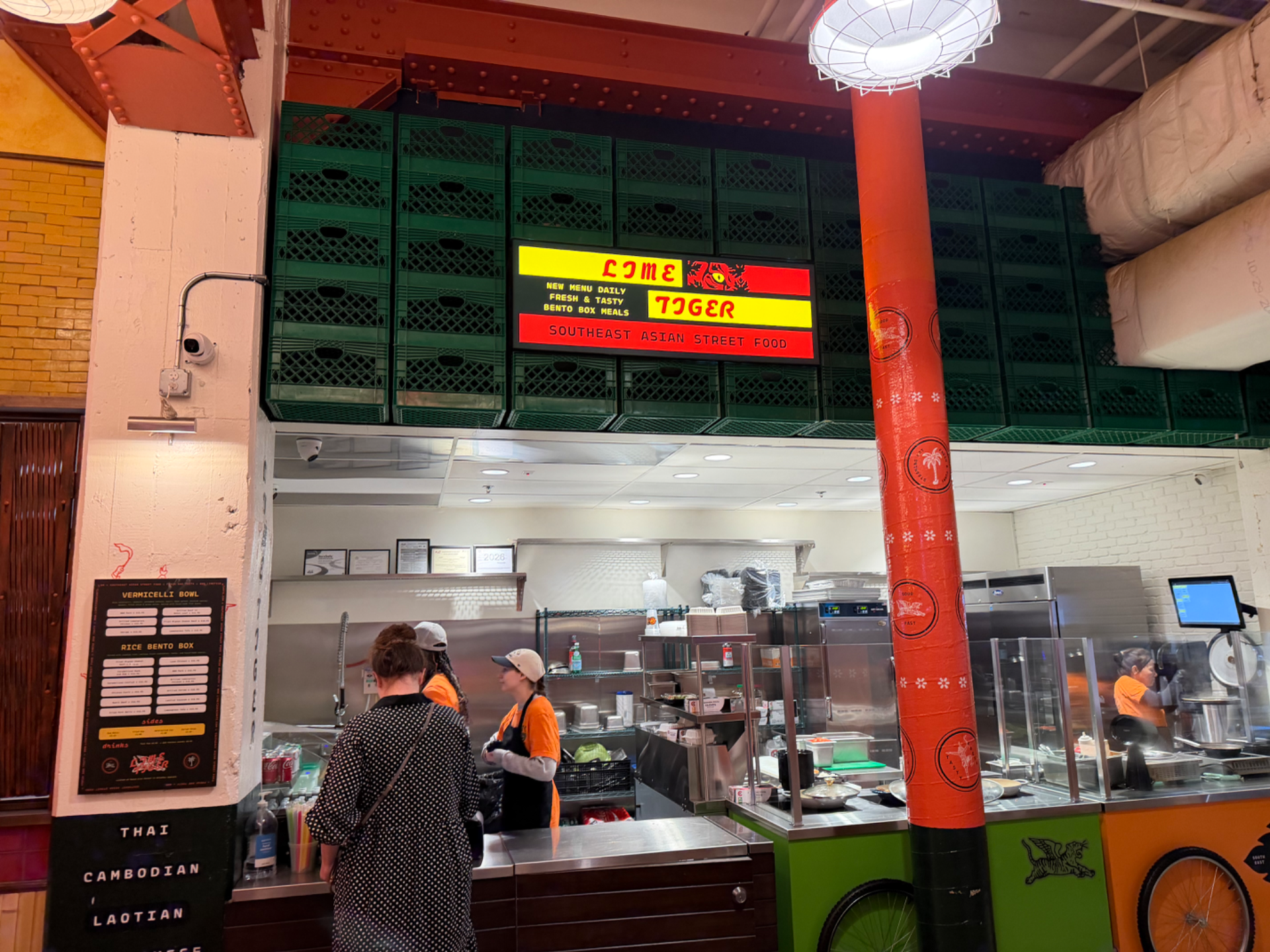 Lime Tiger Southeast Asian street food stall inside a market hall, with customers ordering at a bright open kitchen counter b
